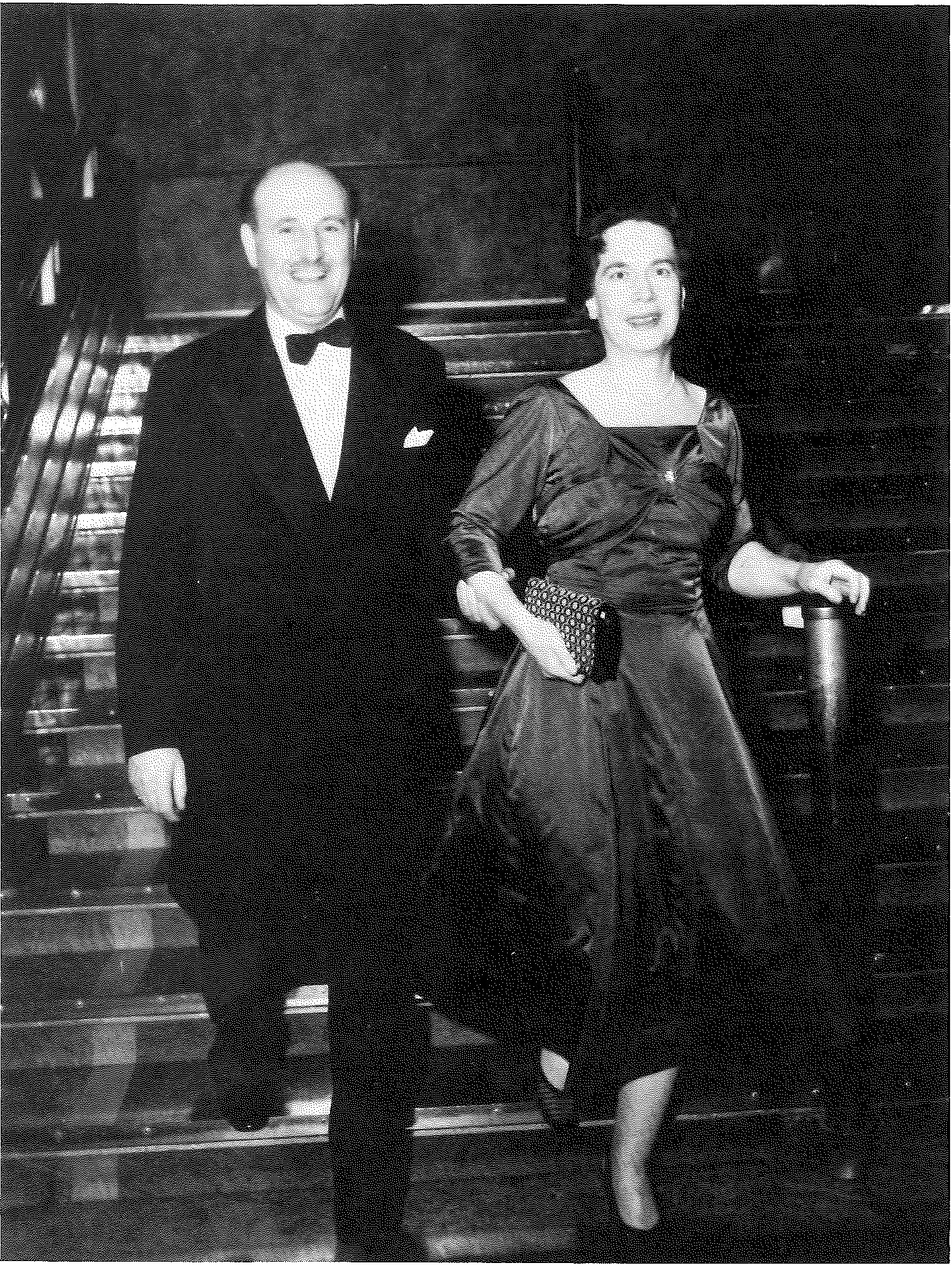 A man in a dinner jacket and a woman in a long evening gown standing together on a ship’s staircase.