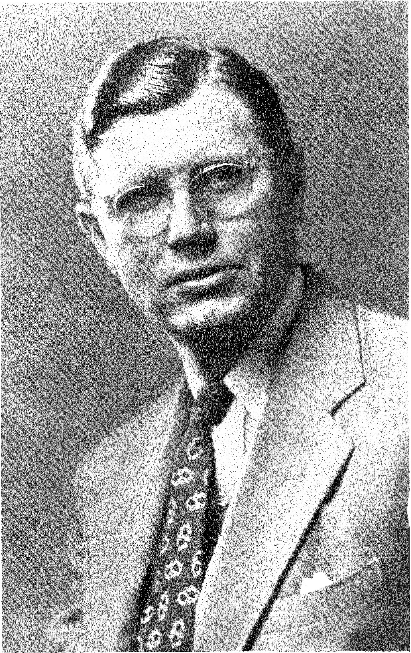 Studio portrait of a man in rimless glasses, a light suit and a patterned tie.