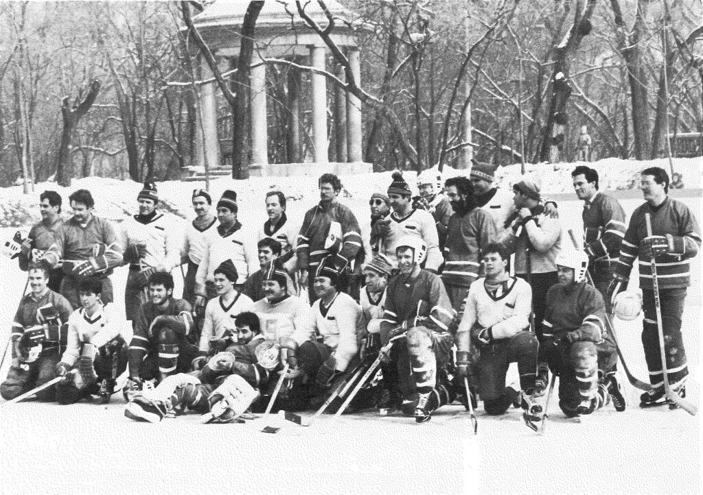 Deux équipes de hockey posent, bâtons à la main, sur une patinoire extérieure bordée d’arbres enneigés.