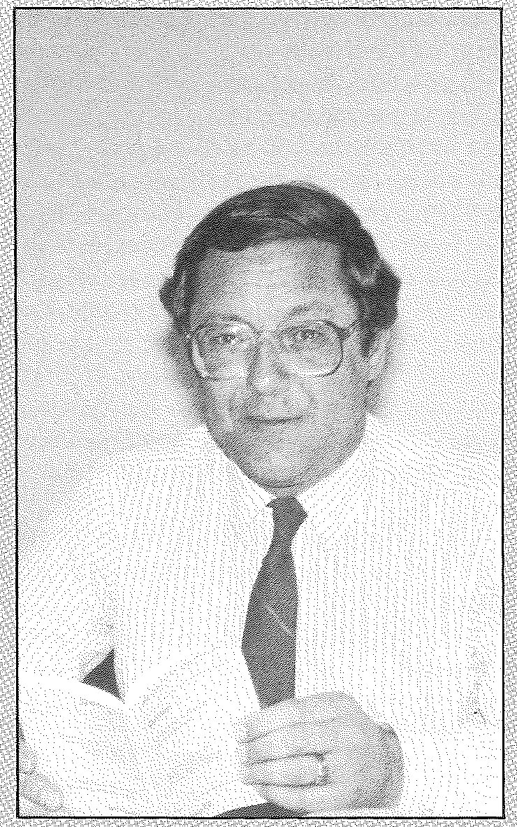 Portrait of a man in glasses and a dark jacket, his hands clasped in front of him.