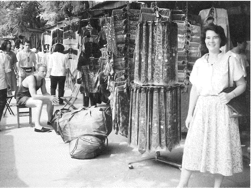 une femme en robe blanche devant les étals de vêtements d’un marché en plein air