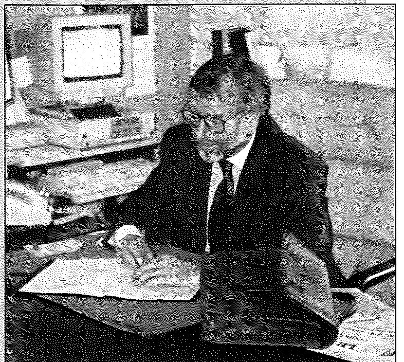 A man at a desk beside an early desktop computer.