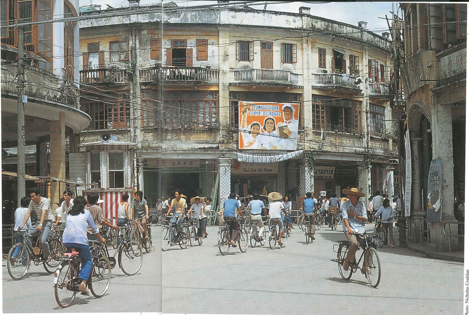 Cyclists crossing an intersection in front of a weathered colonnaded building hung with a painted billboard