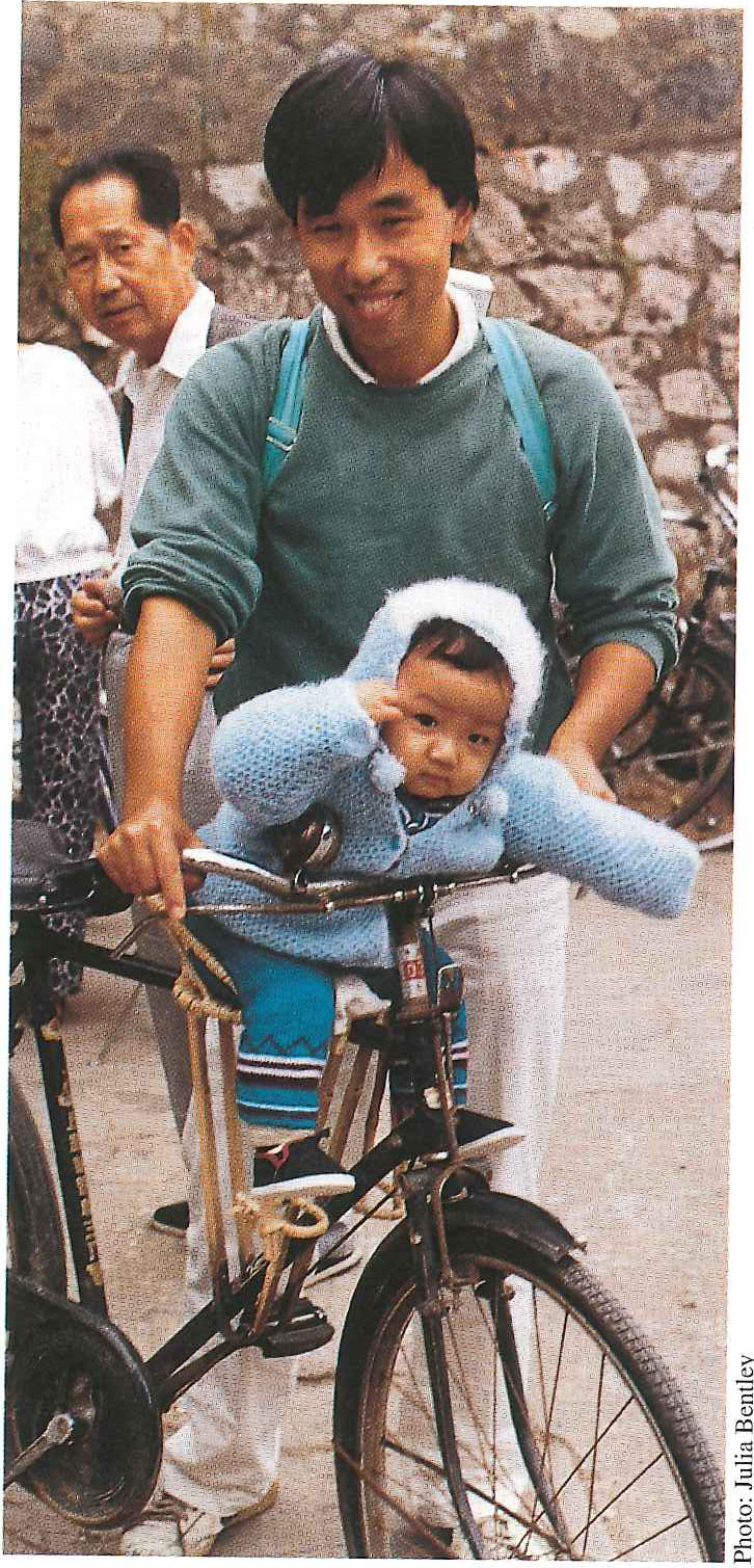 A man standing with his bicycle, a small child in a seat behind the saddle