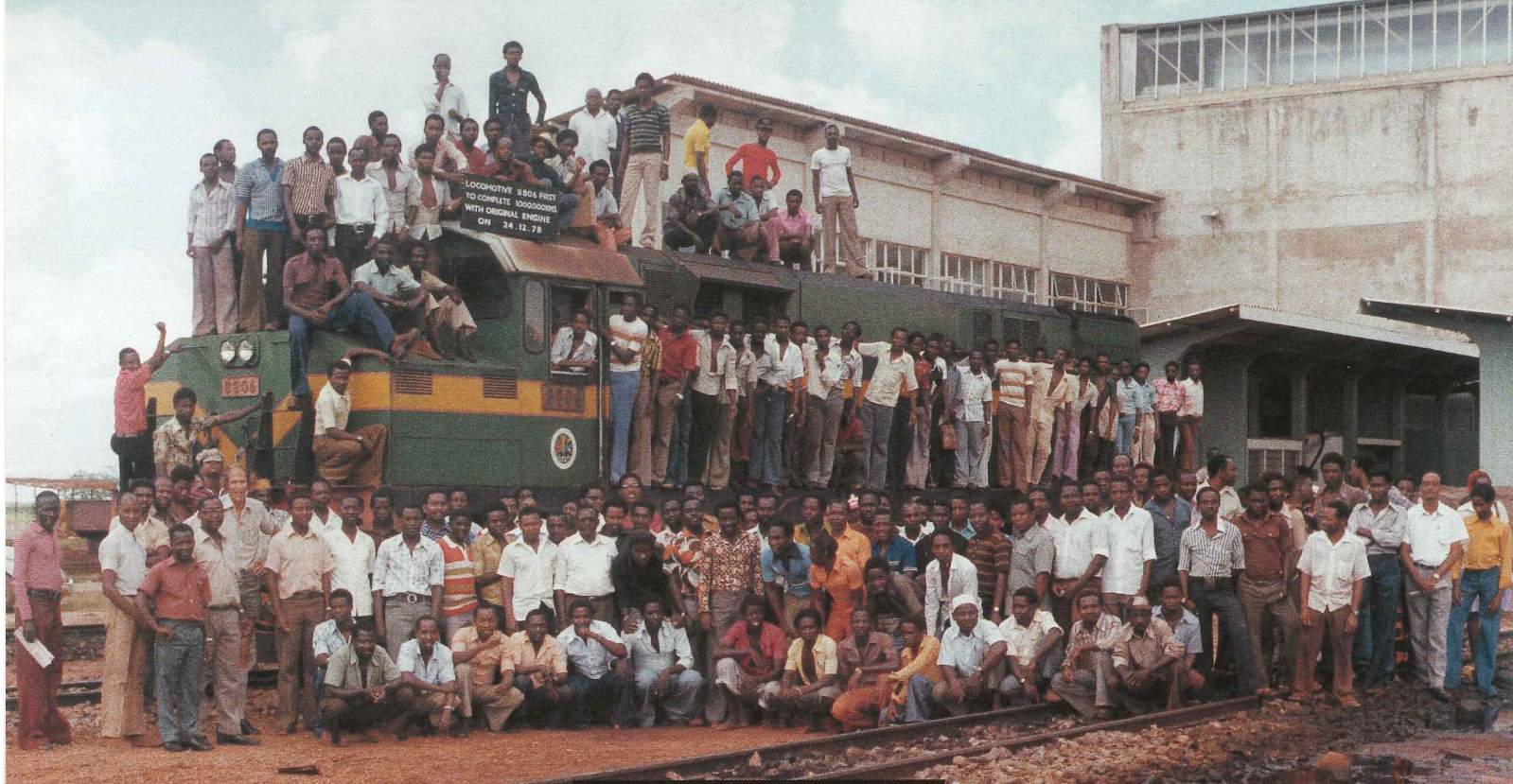 A crowd of railway workers standing on and around a diesel locomotive outside a workshop