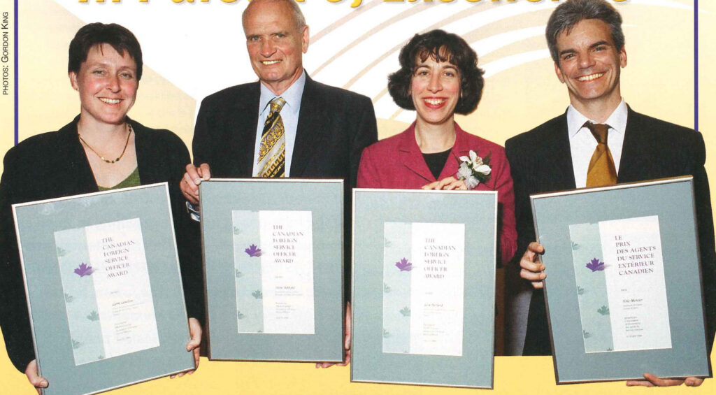 Four award recipients standing side by side, each holding a framed certificate