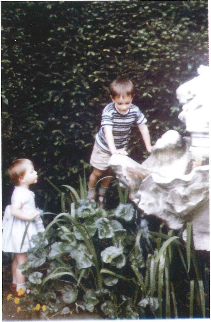 two small children beside a stone fountain in a garden