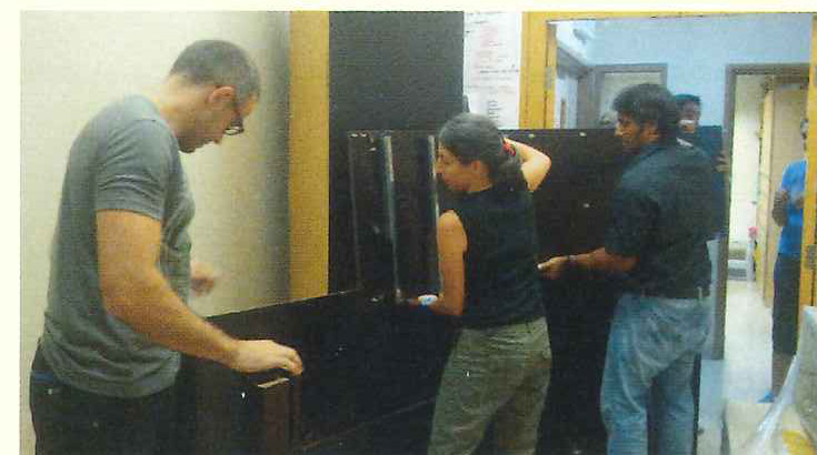 Volunteers manoeuvre a tall storage cabinet away from a wall.