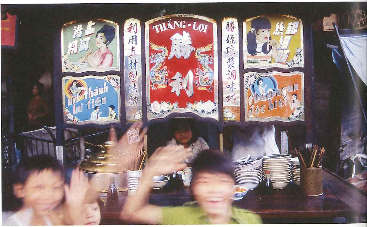 Children waving in front of a shopfront painted with red and gold Chinese signs